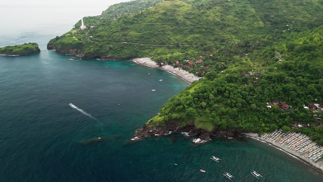 Un video aereo ripreso da un drone mostra un insediamento costiero indonesiano tra ripide montagne boscose e una baia calma e protetta dove numerose piccole barche da pesca sono ormeggiate vicino alla spiaggia rocciosa