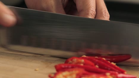 slicing red chili pepper for thai recipe on wooden chopping board using knife