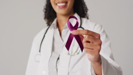 Video-of-smiling-biracial-female-doctor-holding-purple-pancreatic-cancer-ribbon