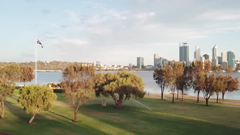 Australian-flag-pole-in-park,-aerial-pedestal-up-to-reveal-city-in-distance