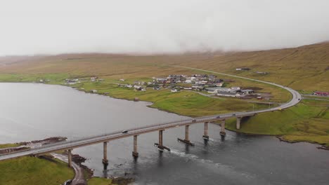 Vista-Aérea-Sobre-El-Fiordo-Y-El-Puente-Hacia-Un-Pequeño-Pueblo-En-Las-Islas-Feroe