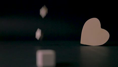 four little wooden blocks drop onto a black table where a standing heart is the main focus