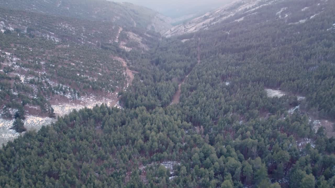 vista aérea que revela un tiro inclinado hacia arriba en un valle durante la puesta de sol en invierno con nieve en los picos de las montañas en madrid, españa