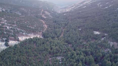 Aerial-view-revealing-tilt-up-shot-in-a-valley-during-sunset-in-winter-with-snow-on-mountain-peaks-in-Madrid,-Spain