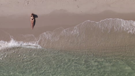 young white woman in bikini sits off center on sandy sea shore beach