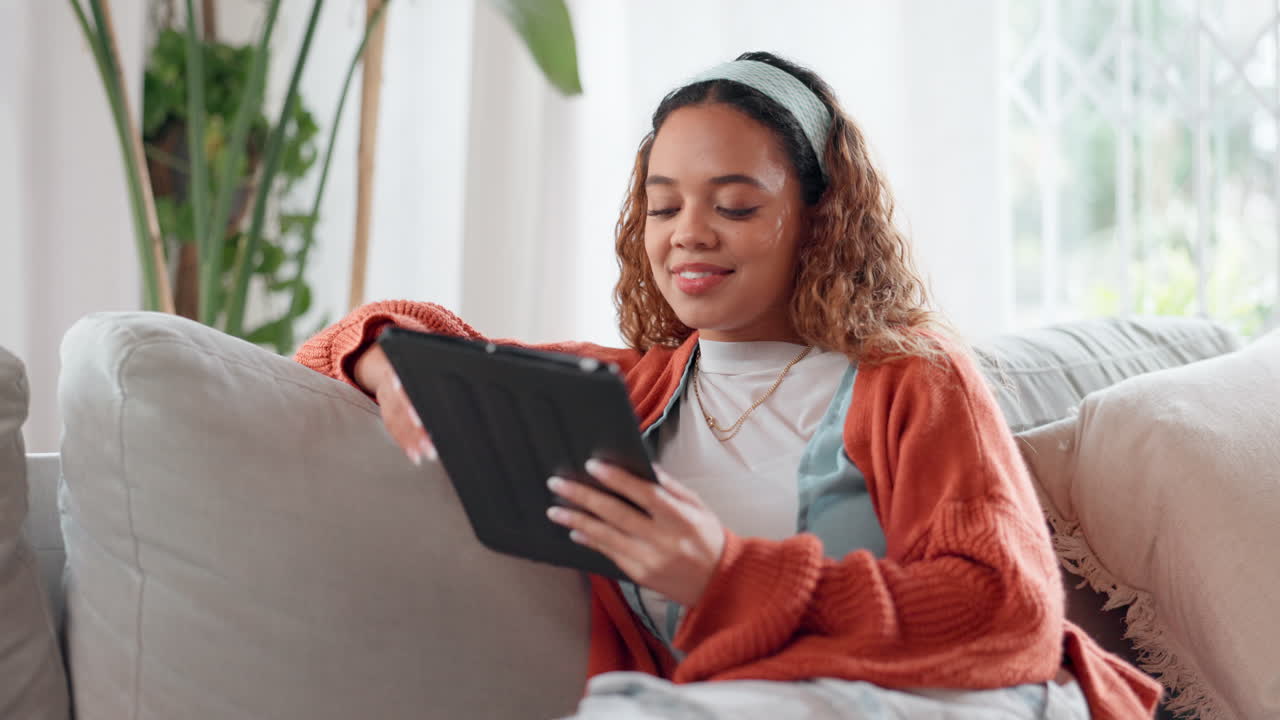 mujer joven riendo mientras usa una tableta en un sofá