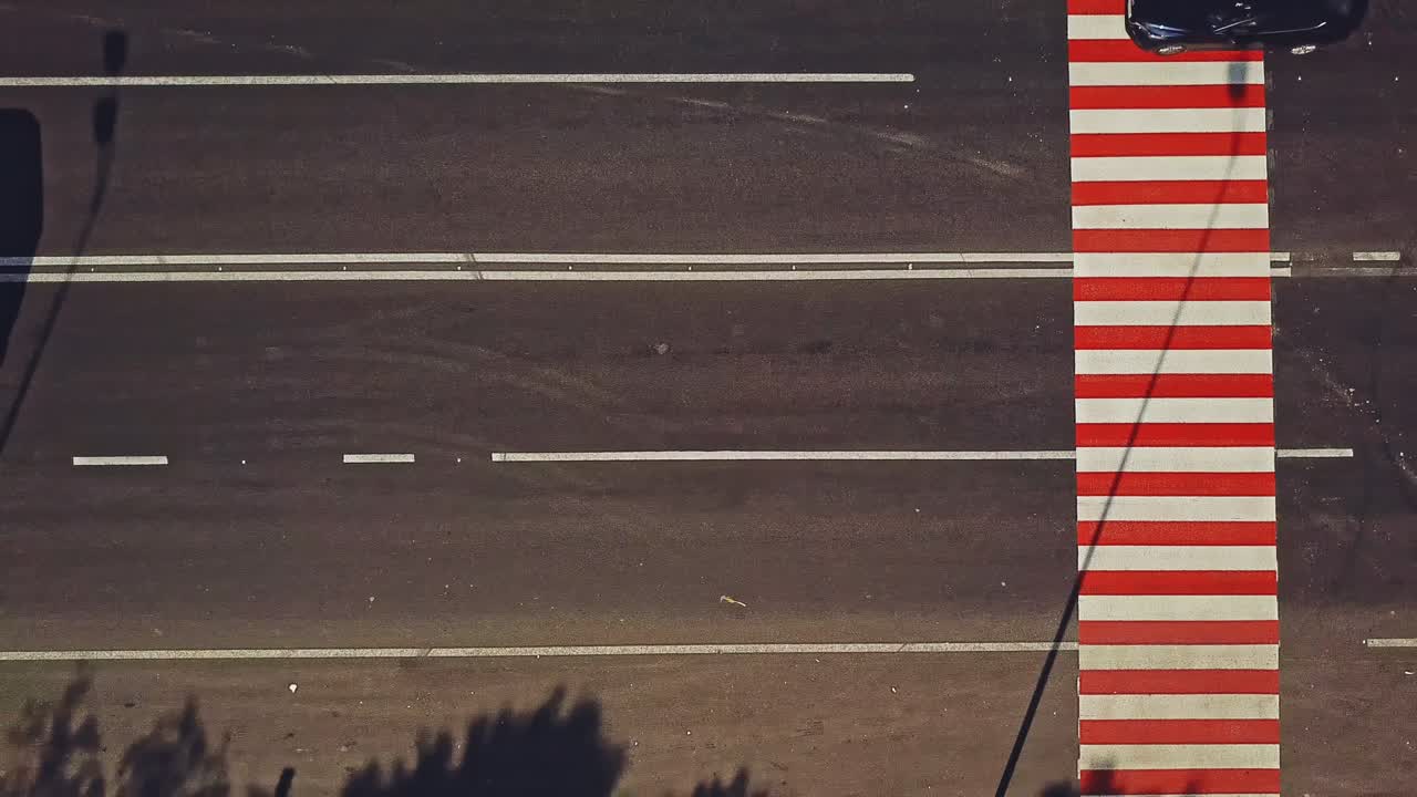 Pedestrian crossing with red and white stripes on the road and cars going by outdoors. Vertical stripes on the road to show drivers the approach of zebra crossing. Camera motion left