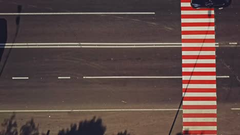 Pedestrian crossing with red and white stripes on the road and cars going by outdoors. Vertical stripes on the road to show drivers the approach of zebra crossing. Camera motion left