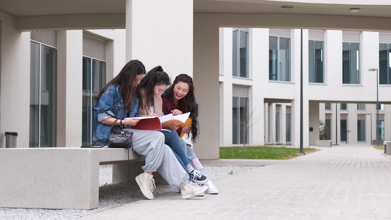 Tre studentesse asiatiche che parlano durante la pausa sedute nel campus