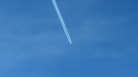 vista lejana de un avión en vuelo dejando estelas blancas contra el cielo azul