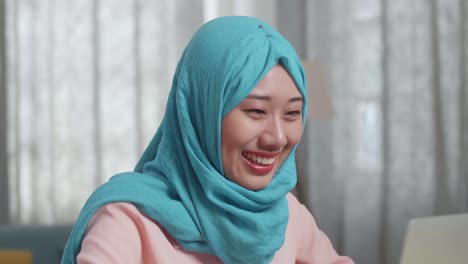 노트북에서 일하는 히자브를 입은 미소 짓는 여자