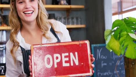 Portrait-of-happy-waitress-is-holding-open-sign