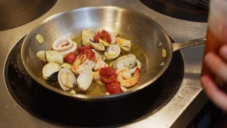 mediterranean seafood dish preparation in professional restaurant kitchen, chef add red fresh cherry tomatoes in a pot