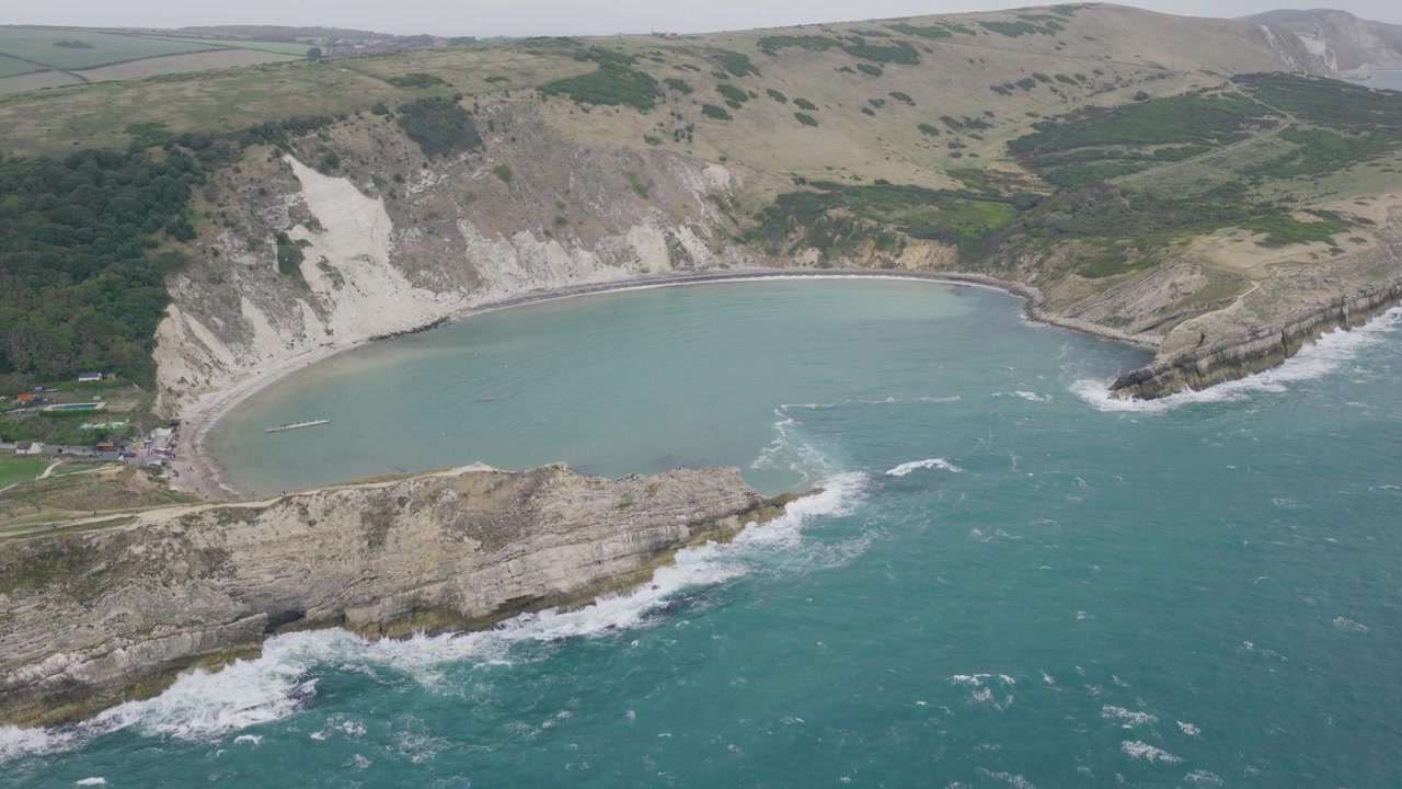 Vista aérea de Lulworth Cove en Dorset que muestra la bahía curva, los acantilados de piedra caliza, el agua turquesa y las olas que entran desde la costa Jurásica