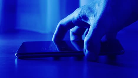 Closeup-Of-Young-Man-Hands-Pick-Up-Phone-From-Desk-At-Night-Blue-Background