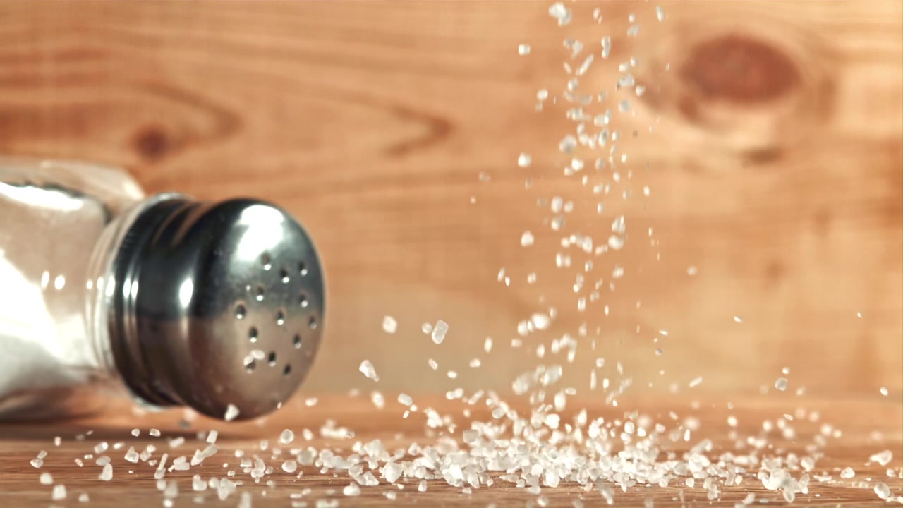 Coarse Salt Falling from Shaker onto Wooden Surface in Slow Motion