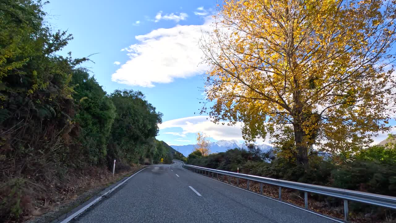 Vehicle drives along winding rural road, autumn trees, clear daylight, smooth forward camera movement, Queenstown