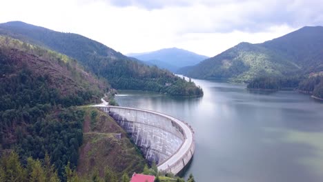 Toma-Aérea-De-Drones-De-Una-Hermosa-Represa-Hecha-Por-El-Hombre-Con-Las-Hermosas-Montañas-Rumanas-Como-Telón-De-Fondo