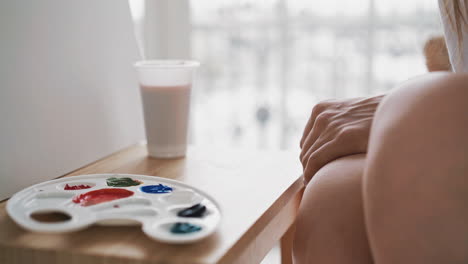 artist sits near palette with paints and cup on wooden easel