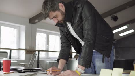 young man working on a project, drawing and thinking in modern office. coffee cup and laptop on the table. shot in 4k.