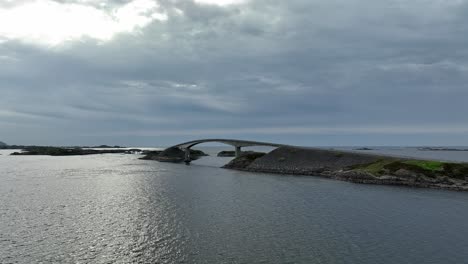 nubes oscuras detrás del puente de storseisundet en la carretera del océano atlántico en noruega - aero sobre el mar mientras se mueve hacia el puente a baja altitud