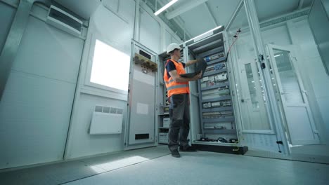 el ingeniero eléctrico que trabaja comprueba la tensión de corriente eléctrica y la sobrecarga en la parte delantera del gabinete del centro de carga o de la unidad de consumo para el mantenimiento en la sala principal del sistema de distribución de energía.