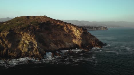 Eine-Luftaufnahme-Der-Point-Dume-Klippen-In-Malibu-In-Kalifornien,-Während-Die-Wellen-Abends-Gegen-Die-Felsen-Schlagen,-Wenn-Die-Pulsierende-Sonnenuntergang-Untergeht