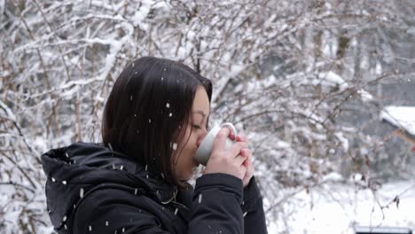 Asiatische-Frau-Trinkt-Bei-Schneefall-Eine-Heiße-Tasse-Tee-Im-Waldgebiet