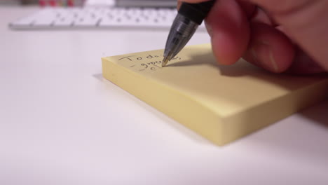 hombre escribiendo una lista de tareas pendientes en un bloc de notas amarillo