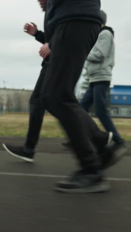 side view of an adult and two young boys jogging together with the same pace on a stadium track, with buildings visible in the background