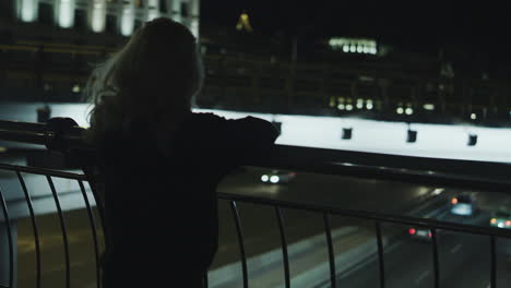 Woman-enjoying-city-view-cars-passing-at-night-street-in-downtown.