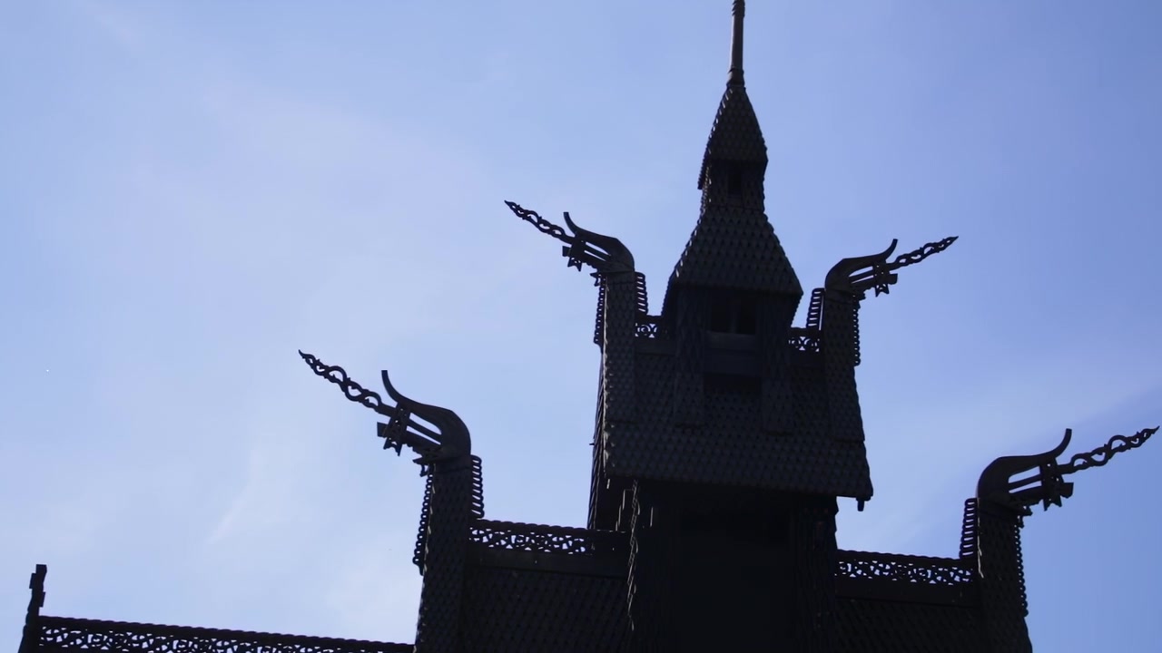 Panorering opad afslører udsmykket trækirke tag med drageskæringer blandt forårstræer i Bergen, Norge.
