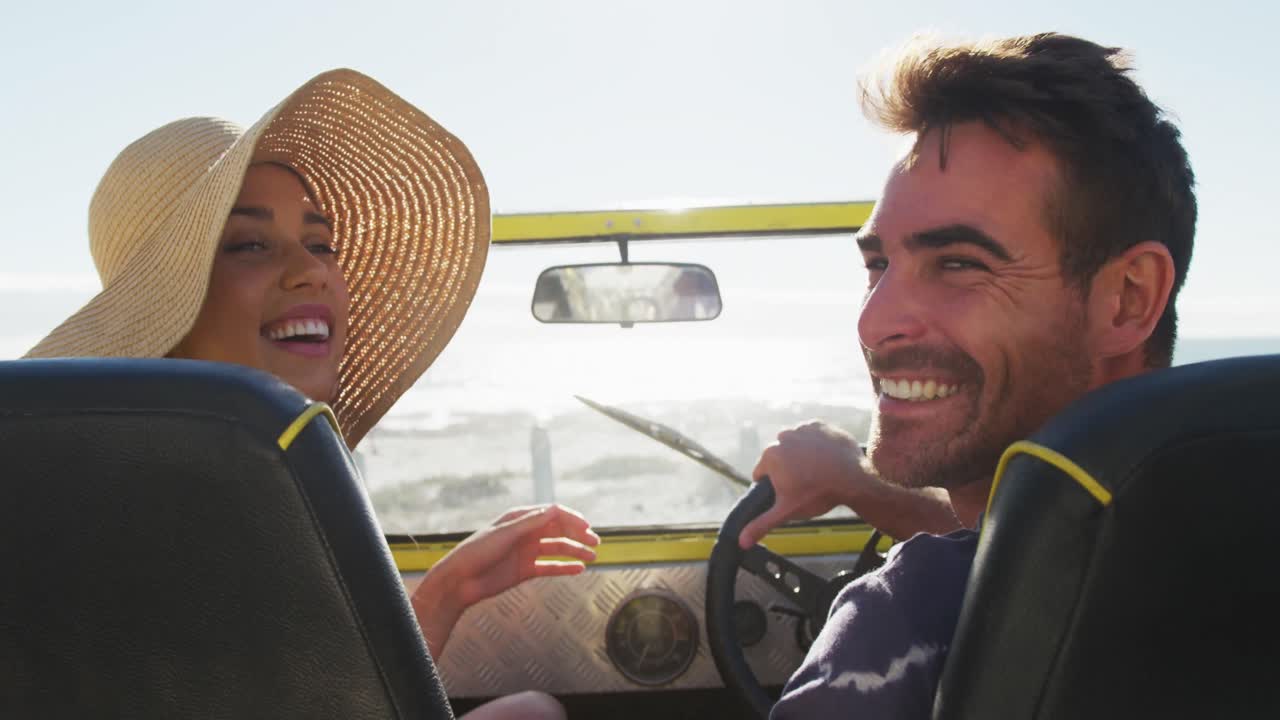 feliz pareja caucásica sentada en un buggy de playa junto al mar hablando