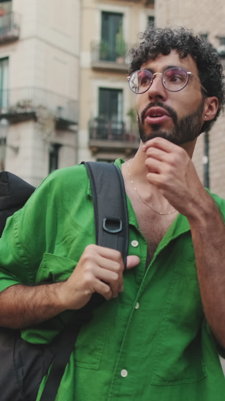 Hombre joven con estilo y mochila mirando a su alrededor en la ciudad