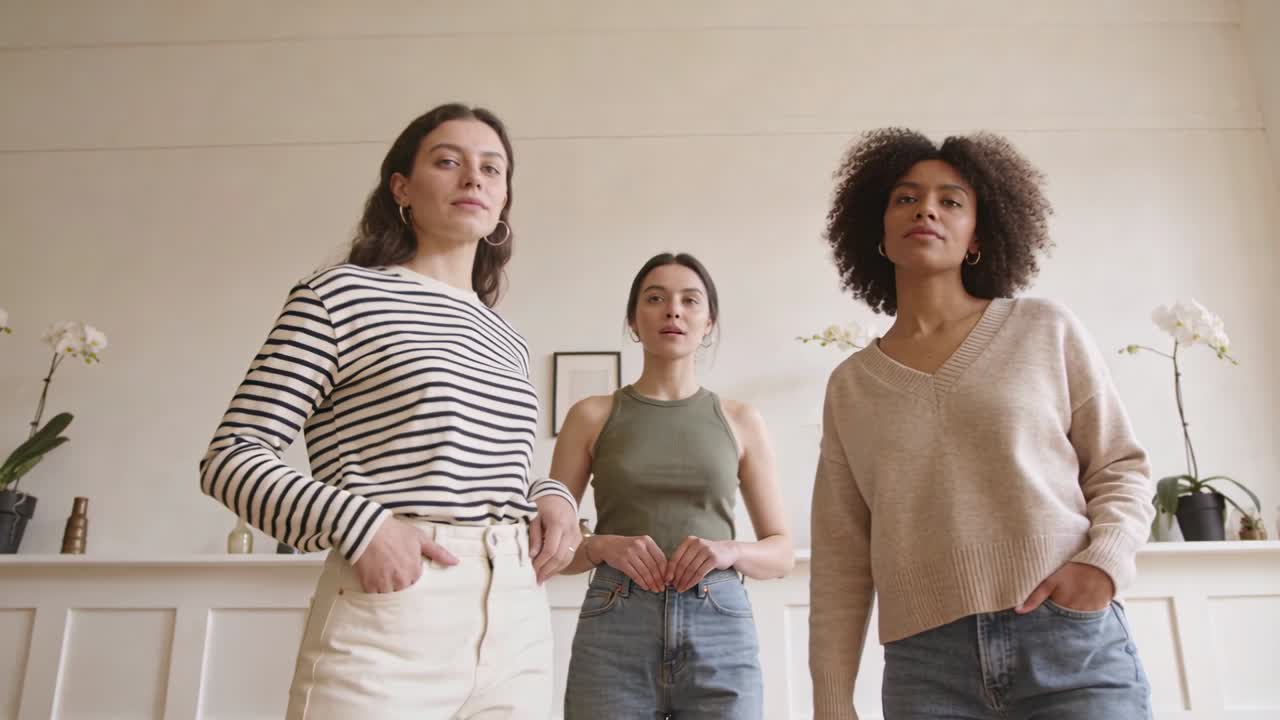 Mulher de jeans movendo-se para o centro, tocando o ombro da mulher à direita, formando uma pose de grupo na lareira.