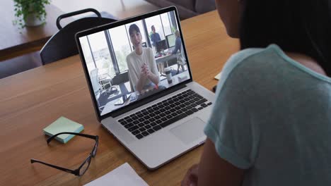 Mixed-race-businesswoman-sitting-at-desk-using-laptop-having-video-call-with-female-colleague