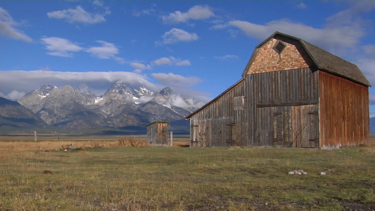 un antiguo granero se encuentra en un campo con la cordillera grand teton en el fondo