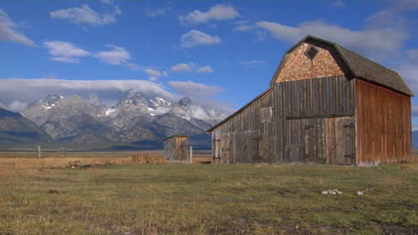 Un-Viejo-Granero-Se-Encuentra-En-Un-Campo-Con-La-Cordillera-De-Grand-Teton-En-El-Fondo