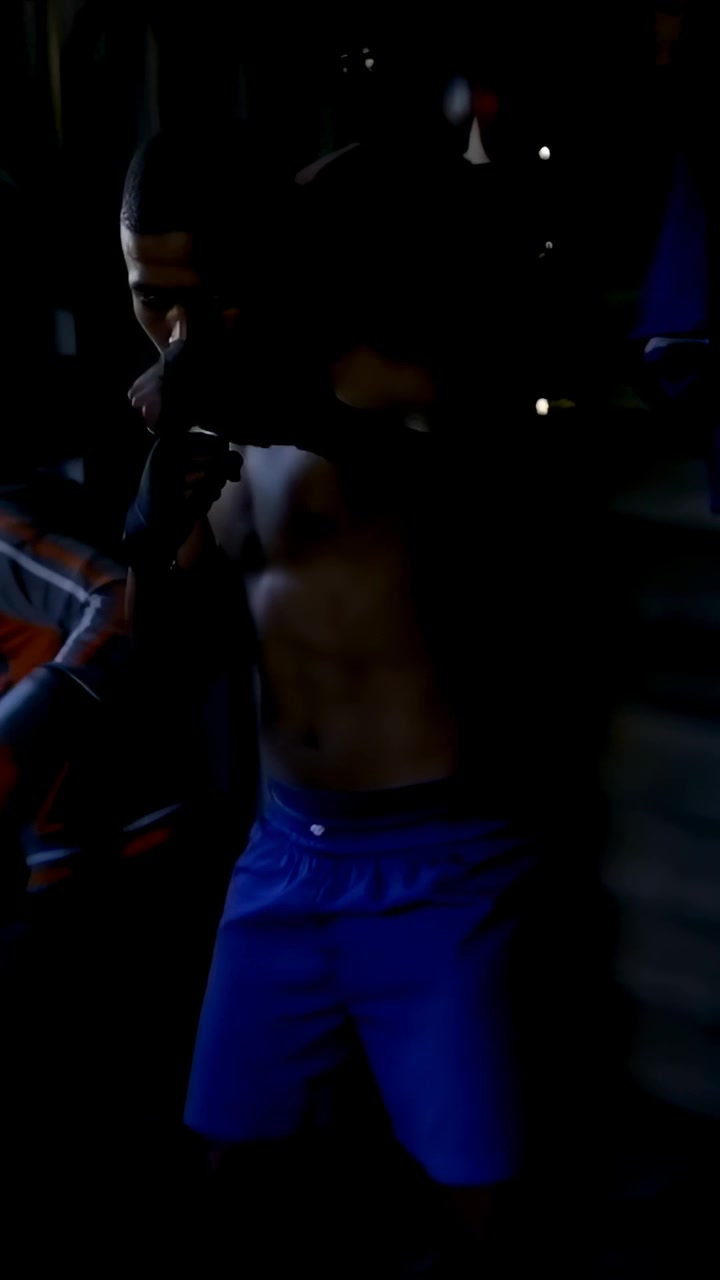 Video verticale: Uomo senza maglietta che si allena e si sistema i guanti mentre un adolescente con la felpa colpisce un sacco in garage