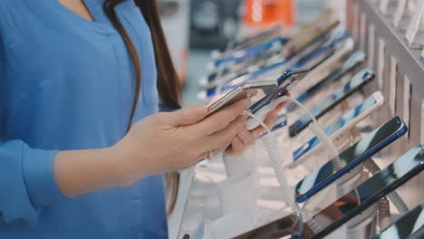 Closeup-of-woman's-hand-choosing-for-buying-a-new-smart-phone-near-a-shop-window-in-an-electronics-store