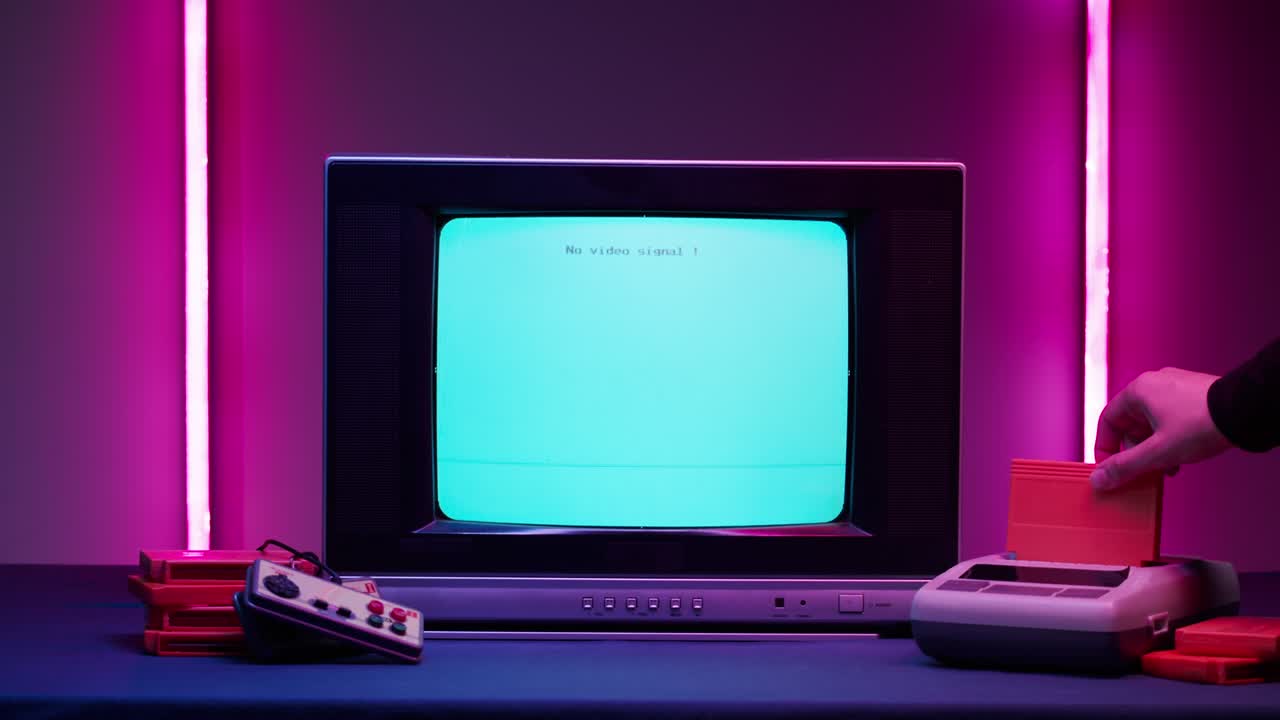 Old television with blue screen on pink neon background. Close-up of vintage tv and retro playstation, changing cartridges. Antique video game, nostalgia