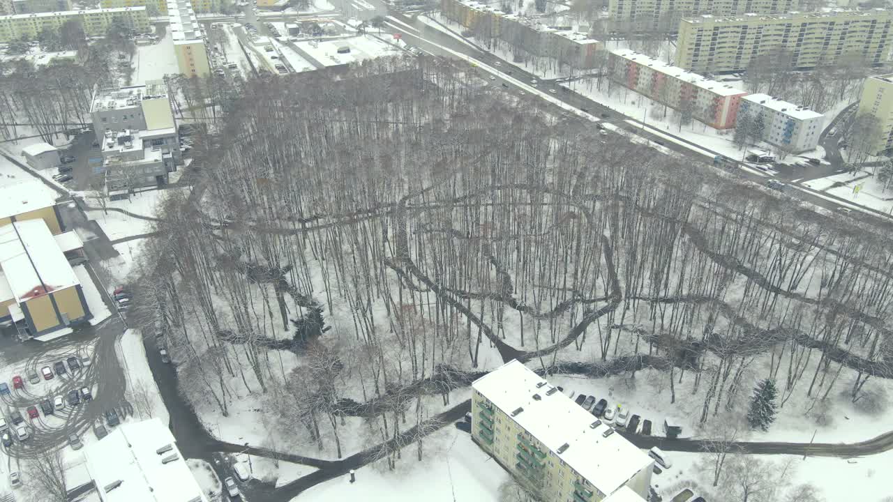 Aerial drone footage of Lepistiku Park in estonia during winter cloudy day that has small narrow and twisting rivers in the park. White snow covering the ground around roads and a TTG school building.