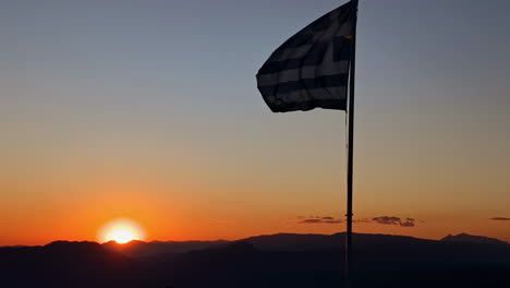 greek flag blowing in the wind over the mountain countryside at sunset