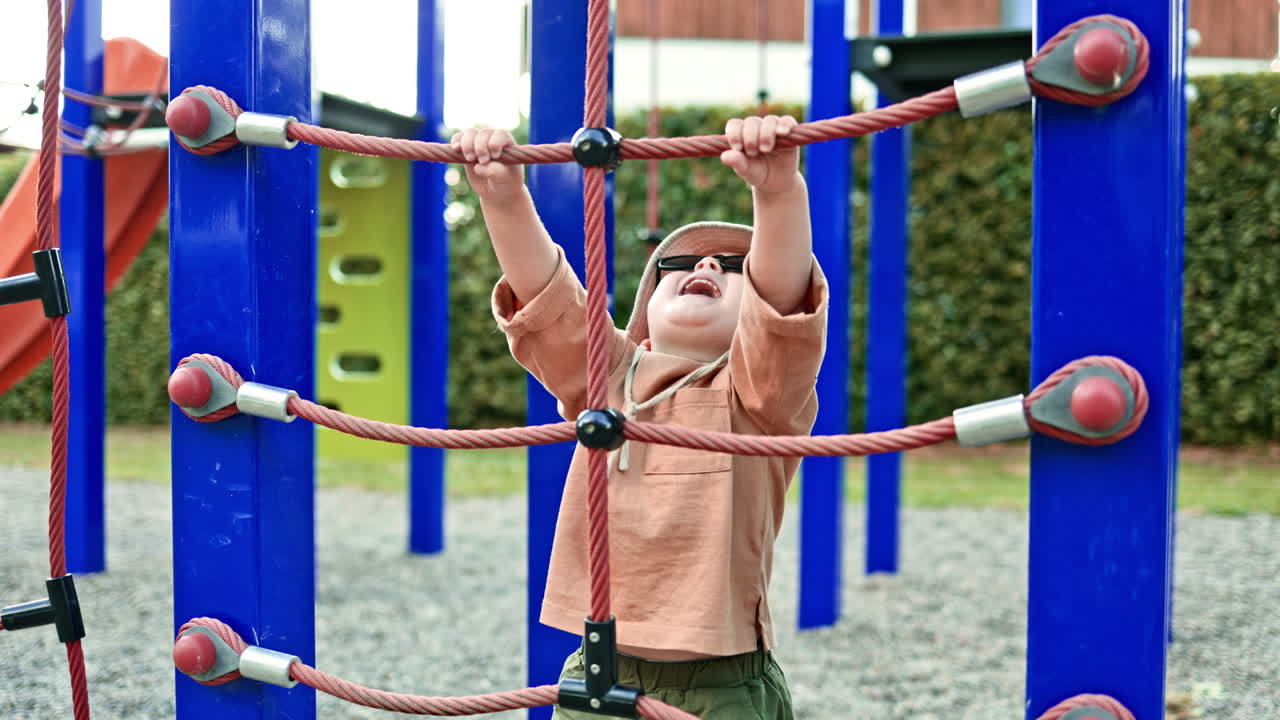 Cheerful toddler in sunglasses playing on playground. Child in panama hat on head running on playground in city park. Child exploring environment. Child playing independently on playground