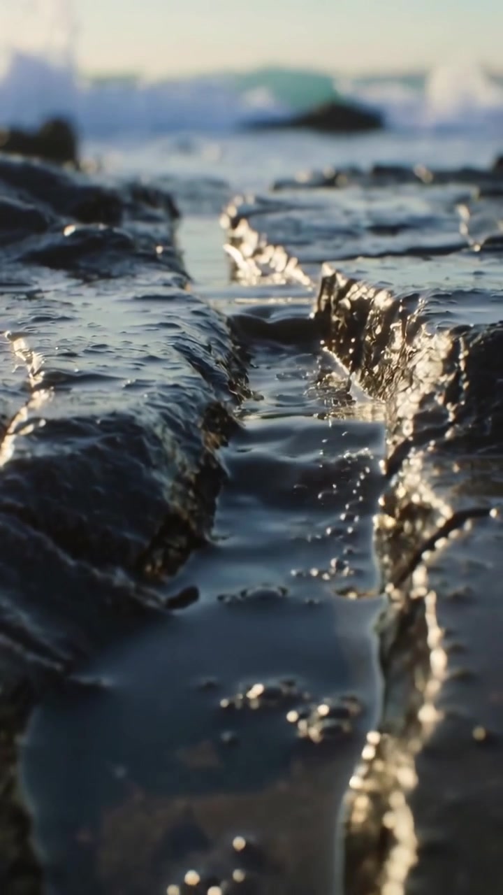 Video verticale: Onde impetuose che spingono l'acqua in uno stretto canale roccioso scuro sulla riva, creando schizzi