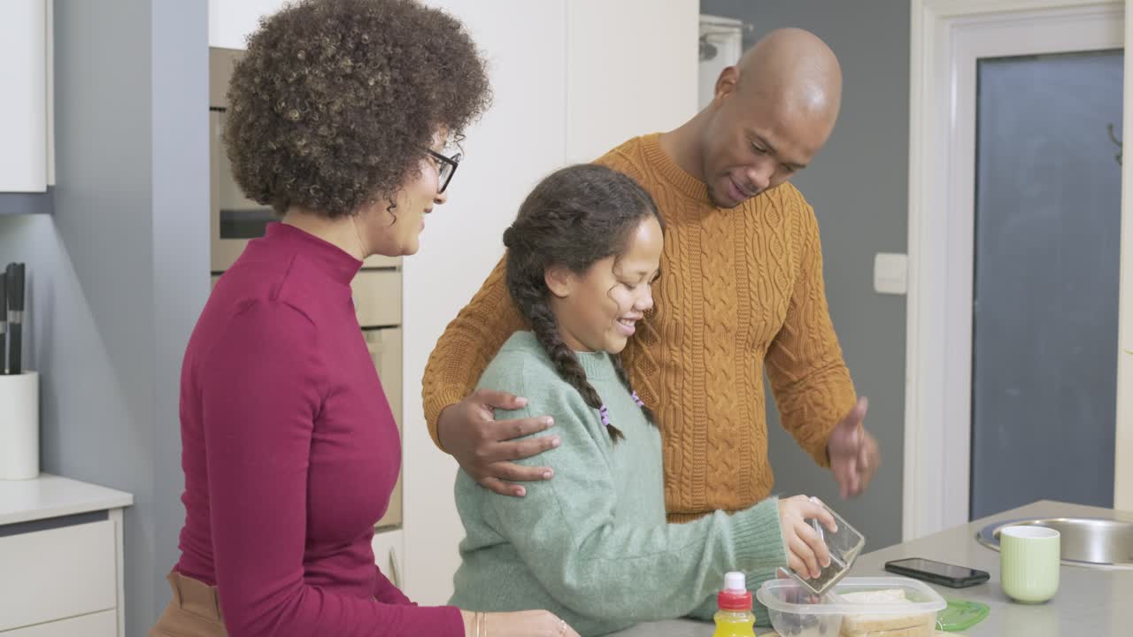 Parents guiding daughter and adding sliced bread and berries into box for school at kitchen island