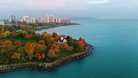Aerial-view-over-the-fall-colored-Promontory-Point,-toward-the-hazy-skyline-of-Chicago