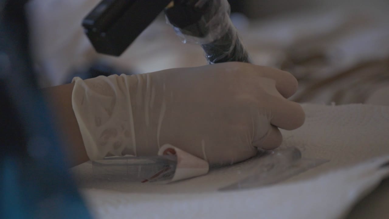 Hands Of A Tattoo Artist With Disposable Gloves Getting Ink On The Needle Of A Handheld Tattoo Machine - close up slowmo