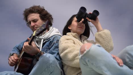 a young boy plays the guitar and a young girl looks around with a pair of binoculars on the roof of a caravan.