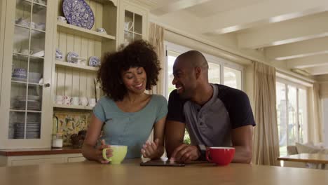 Happy-mixed-race-couple-drinking-coffee-in-their-kitchen